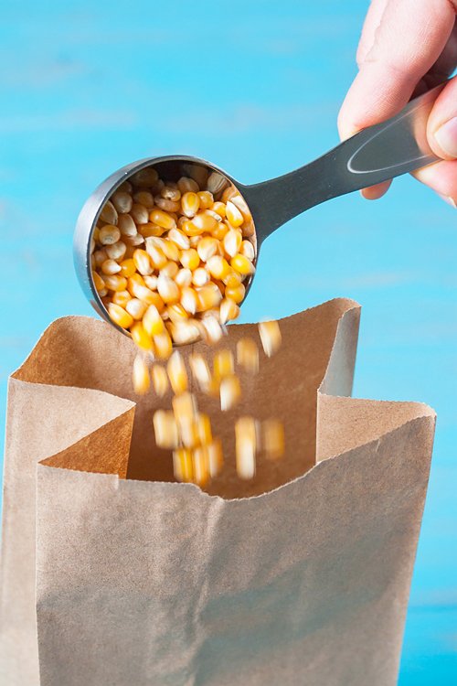 Pouring popcorn in a brown bag to microwave for popcorn